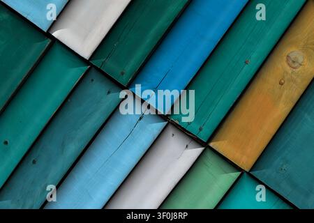 Diagonales Muster aus farbig bemalten Holzpaneelen mit grünen, blauen, gelben und weißen Tönen, das natürliche Texturen und abgeschrägte Kanten zeigt Stockfoto
