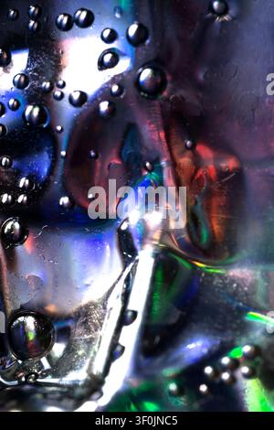 Makroabstrakt von Wassertröpfchen auf reflektierendem Metallglas, mit lebhaften blauen, grünen, roten und weißen Lichtreflexionen, die eine futuristische Textur erzeugen. Stockfoto