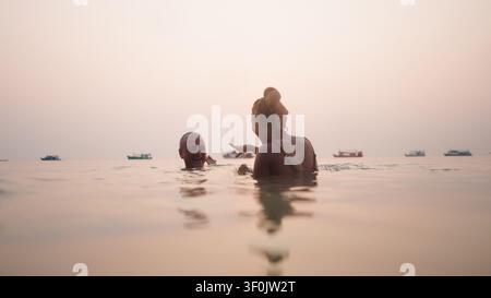 Paar genießt fröhliches Schwimmen und lacht zusammen im Meer bei Sonnenuntergang Stockfoto