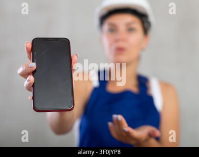 Junge Ingenieurin, Architektin im Bau Overall und Sicherheitshelm mit Handy-Bildschirm Stockfoto