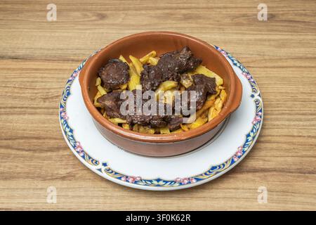 Traditioneller spanischer Rindereintopf mit dicken Pommes, serviert in einer Tonschale auf einem dekorativen Blumenteller Stockfoto