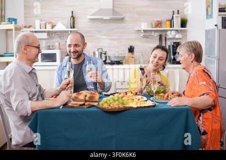 Vater und Sohn halten Weingläser während des Brunch zu Hause am Esstisch, kombiniert mit Wein, Essen, familiärer Verbindung und alltäglicher Beziehungsgeschichtenerzählung. Stockfoto