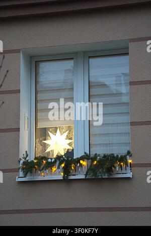 Weihnachtsfensterdekoration beleuchteter Stern und Girlande, in der Fassade eines Wohngebäudes, mit beleuchtetem Stern, Girlande mit Lichtern, Fensterrollos, l Stockfoto