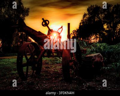 Ein Vintage-Traktor steht auf einer Cottage-Gartenwiese und fängt das Sonnenlicht mit Lichtstrahlen ein, die durchscheinen Stockfoto