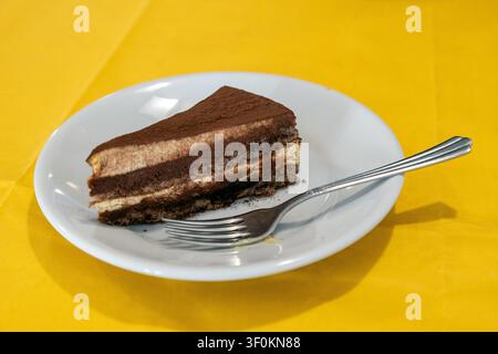 Eine Scheibe Tiramisu, serviert in einem Restaurant auf einem weißen Teller mit einer Gabel auf einer gelben Tischdecke, Chioggia, Veneto, Italien Stockfoto
