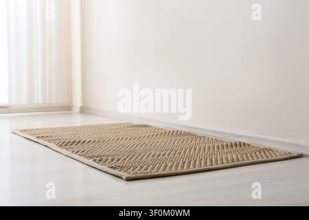 Brauner gewebter Teppich auf hellem Holzboden in einem minimalistischen Raum mit weißen Wänden und durchsichtigen Vorhängen, dieses saubere und moderne Innendesign bietet eine neutrale Stockfoto