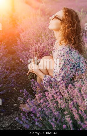 Lavendel-Frau-Blumen, junge Frau sitzt in einem Lavendelfeld und hält einen Blumenstrauß, während sie einen friedlichen sonnigen Sommernachmittag in der Provence genießt Stockfoto