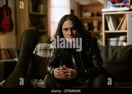 Porträt eines langhaarigen männlichen Musikers, der zu Hause für die Künstler-Branding sitzt Stockfoto
