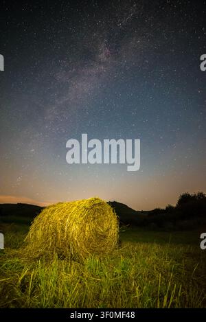 Ein einzelner runder Heuballen wird von künstlichem Licht auf einer grünen Wiese beleuchtet. Stockfoto