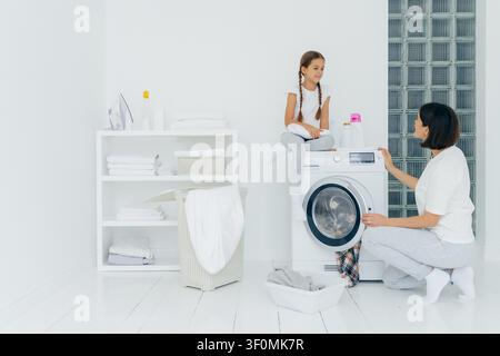 Mutter und Tochter waschen gemeinsam neben der Waschmaschine in einem hellen weißen Waschraum Stockfoto