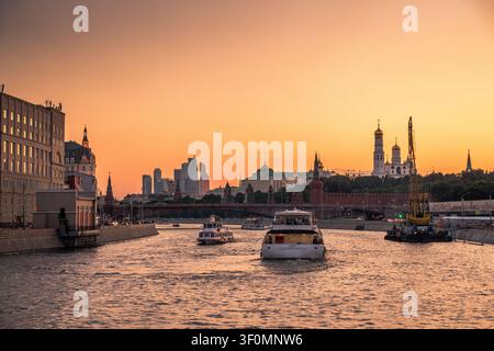 Passagier-Kreuzfahrtschiffe navigieren auf der Moskwa in Richtung des ikonischen Moskauer Kremlkomplexes, mit dem GlockenTurm Ivans des Großen, dem Großen KremlPalast. Stockfoto