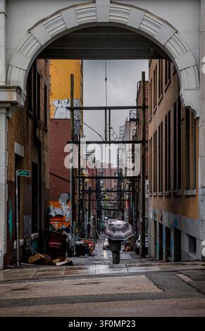 Person mit einem Regenschirm geht durch eine Gasse im Downtown Eastside an einem nieselregenartigen Nachmittag in Vancouver, British Columbia, Kanada. Stockfoto