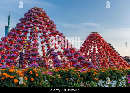 Turmhohe pyramidenförmige Blumeninstallationen, bedeckt mit Hunderten von roten hängenden Töpfen, die vor lila und rosa Petunien platzen, erheben sich über einen Vordergrund von Stockfoto