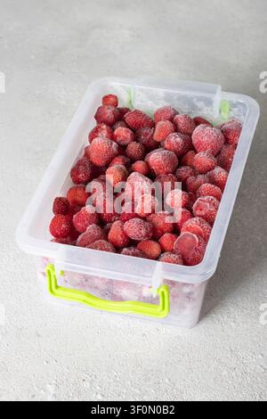 Gefrorene Erdbeeren in den Aufbewahrungsboxen auf grauem Hintergrund Stockfoto