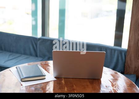 Moderner Arbeitsplatz mit Laptop, Notizbuch und Dokumenten auf Holztablett in der Nähe eines Panoramafensters in einem Café. Arbeitsplatz für Telearbeit, Freelancing, Geschäft p Stockfoto