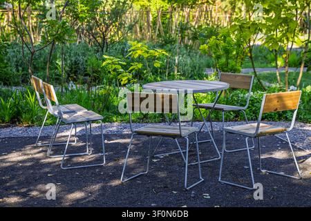 Sitzbereich eines Outdoor-Cafés mit Holzstühlen und Metalltisch inmitten üppiger Grünpflanzen Stockfoto