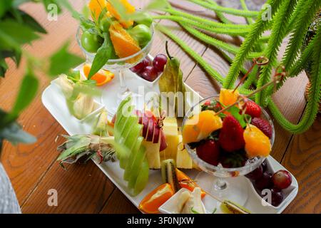 Ein Obstteller zeigt verschiedene frische Früchte, die in Schalen arrangiert sind. Trauben, Orangen, Erdbeeren und Kiwi werden auf einem Holztisch zum Verzehr präsentiert Stockfoto