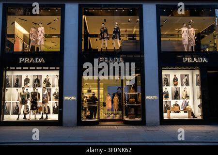 Ein mehrstöckiges Prada-Flaggschiffgeschäft zeigt beleuchtete Modefenster, Schaufensterpuppen, Kampagnenbilder, Handtaschen und Kleidung in der New Bond Street in Mayf Stockfoto