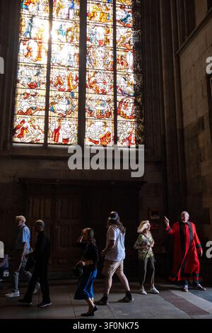 Innenansicht von Besuchern, die unter einem großen Buntglasfenster im Kölner Dom in Köln, Nordrhein-Westfalen, Deutschland vorbeigehen Stockfoto