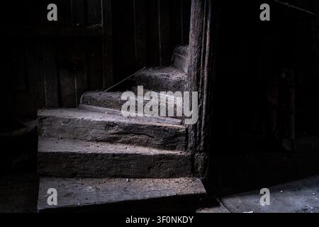 Innensicht einer antiken hölzernen Wendeltreppe mit dunkler Wandvertäfelung, Staub und Brandspuren im Holz im Maison de la Mere Pourcel Stockfoto