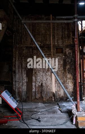 Innenansicht einer mit Feuer markierten Holzwand mit Metallgerüst, einem elektrischen Stromkasten und Stromkabeln im Inneren der Maison de la Mere Pourcel conser Stockfoto