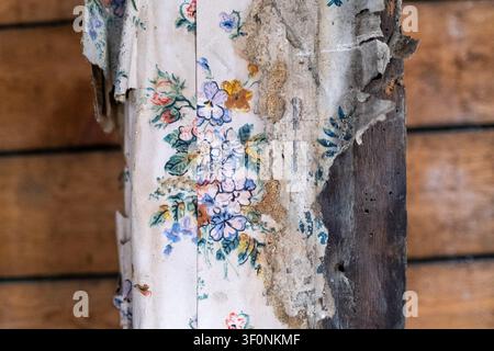 Nahaufnahme von abblätternder Blumentapete, freigelegtem Putz und einem zerfallenen Holzpfosten im Maison de la Mere Pourcel-Konservierungs- und Rekonstruktionsgebäude Stockfoto