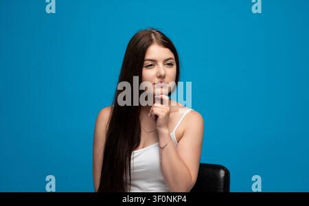 Junge Frau denkt nach, blickt zur Seite mit der Hand am Kinn, brainstormt Ideen, zeigt tiefes Nachdenken und Überlegung Stockfoto