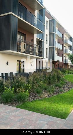 Außenansicht eines neuen Wohnkomplexes mit mehreren Stockwerken, stilvollen Balkonen, einem üppigen Garten und einem Gehweg Stockfoto
