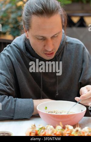 Mann genießt Nudeln in einem gemütlichen asiatischen Restaurant mit glückseliger Freude. Typ erlebt den Geschmack des Moments und genießt warmes Komfortessen. Achtsames Essen in friedlicher Atmosphäre Stockfoto