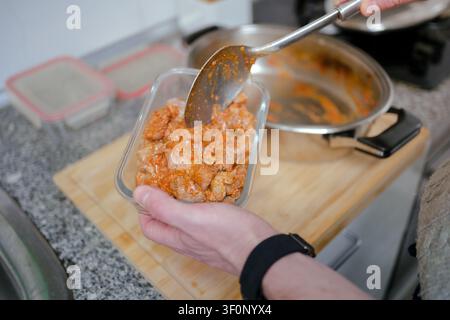 Person, die gesunde Mahlzeitportionen zubereitet, überträgt gekochtes Fleisch mit Sauce in einen Glasvorratsbehälter Stockfoto