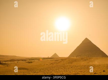 Pyramiden von Gizeh, antikes Wunder, das in der weiten Sahara-Wüste unter einer glühenden Sonne und dramatischem bernsteinfarbenem Himmel steht, perfekt für Ägyptenreisen und Welterbe Stockfoto