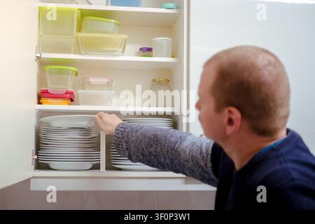 Mann, der Teller und Lebensmittelbehälter in einem ordentlichen Küchenschrank arrangiert Stockfoto