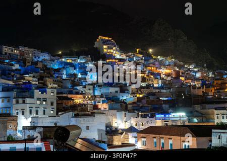 Ein weiter Panoramblick bei Nacht auf die Medina zeigt Gebäude, die in warmem Kunstlicht gegen den tiefblauen Himmel leuchten, mit Laternen und Straßenlaternen Stockfoto