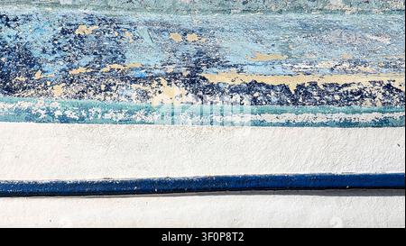Nahaufnahme einer alten verwitterten Wand mit abblätternder blauer und weißer Farbe, die Textur, Verfall, Risse und Farbablöschungsdetails auf einer rustikalen Oberfläche zeigt Stockfoto