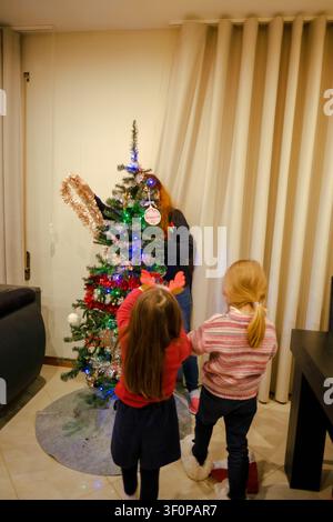 Familienmitglieder schmücken einen festlichen Weihnachtsbaum mit Ornamenten, Lichtern und Lametta in einem Haus Stockfoto