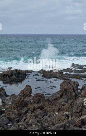 Dramatische vertikale Aufnahme von Meerspritz, die von einer Küstenfelsenformation explodiert, ideal für Öko-Tourismus, Naturliebhaber und Abenteuerkonzepte. Stockfoto