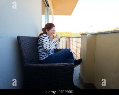 Frau genießt einen friedlichen Morgen, lacht beim Kaffeetrinken auf einem Balkon Stockfoto
