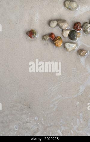 Bunte Kieselsteine auf sandigem Strand mit flachem Wasser, natürlicher Sommerhintergrund mit Kopierraum Stockfoto