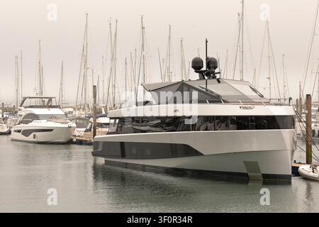 Zwei große Motoryachten liegen in einer Marina mit vielen Segelbooten im Hintergrund an einem grauen, bewölkten Tag Stockfoto
