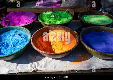 Sechs große Schüsseln, gefüllt mit leuchtend bunten Pigmentpulvern wie Fuchsia, Hellgrün, Blau, Orange und Lila, sind auf einem weiß Tuch bedeckten Arrangement angeordnet Stockfoto