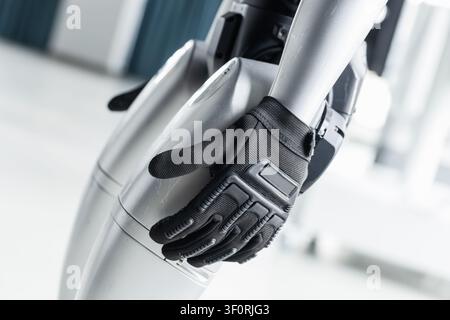 Nahaufnahme eines robotischen Arms, der einen schwarzen taktischen Handschuh trägt, wobei das mechanische Design, der Griff und die Präzision in einer hellen Laboreinrichtung hervorhoben werden, die Stockfoto