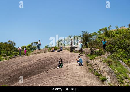 Menschen genießen einen sonnigen Tag auf dem felsigen Aussichtspunkt Pedra Redonda mit einheimischer Vegetation unter einem sommerlichen, sonnigen, klaren blauen Himmel. Stockfoto