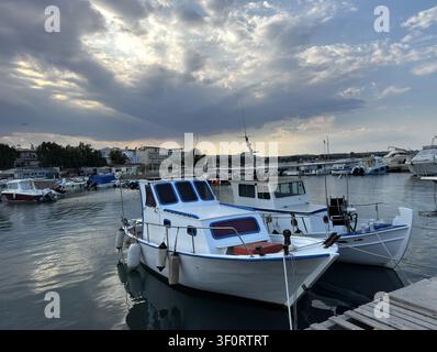 Traditionelle Fischerboote, die im Hafen von Artemida, Attika, Griechenland, unter dramatischen Abendwolken und ruhigen Mittelmeerwasser festgemacht sind Stockfoto