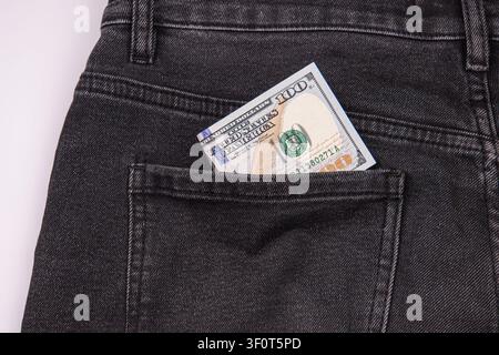 100-Dollar-Schein in der Jeans-Tasche, Fokus auf das Konzept der Wirtschaft, dunkle Denim-Textur, finanzielle Symbolik, minimalistischer Studiohintergrund, saubere Komposition Stockfoto
