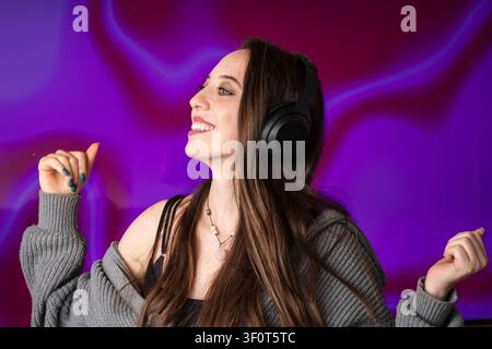 Fröhliche junge Frau tanzt zu ihrer Lieblingsmusik und trägt drahtlose Kopfhörer Stockfoto
