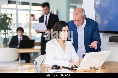 Weibliche Bankmanagerin sitzt am Schreibtisch mit einem älteren Chef davor Stockfoto