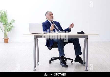 Alter Geschäftsmann Yoga Übungen im Büro Stockfoto