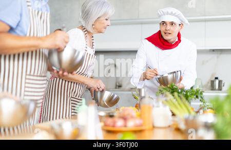 Kochkurs, Essen und Leute Konzept - fröhliche Gruppe von Freunden und männlicher Koch kochen in der Küche Stockfoto