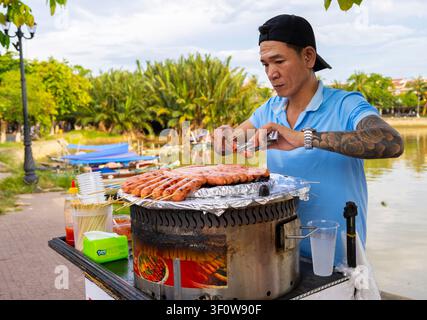 Hoi An, Vietnam – 28. Juni 2025: Ein vietnamesischer Mann bereitet traditionelle Würste auf Spießen zu. Stockfoto