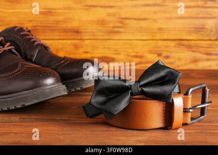 Stylischer schwarzer Fliege, Gürtel und Schuhe auf Holzunterlage Stockfoto